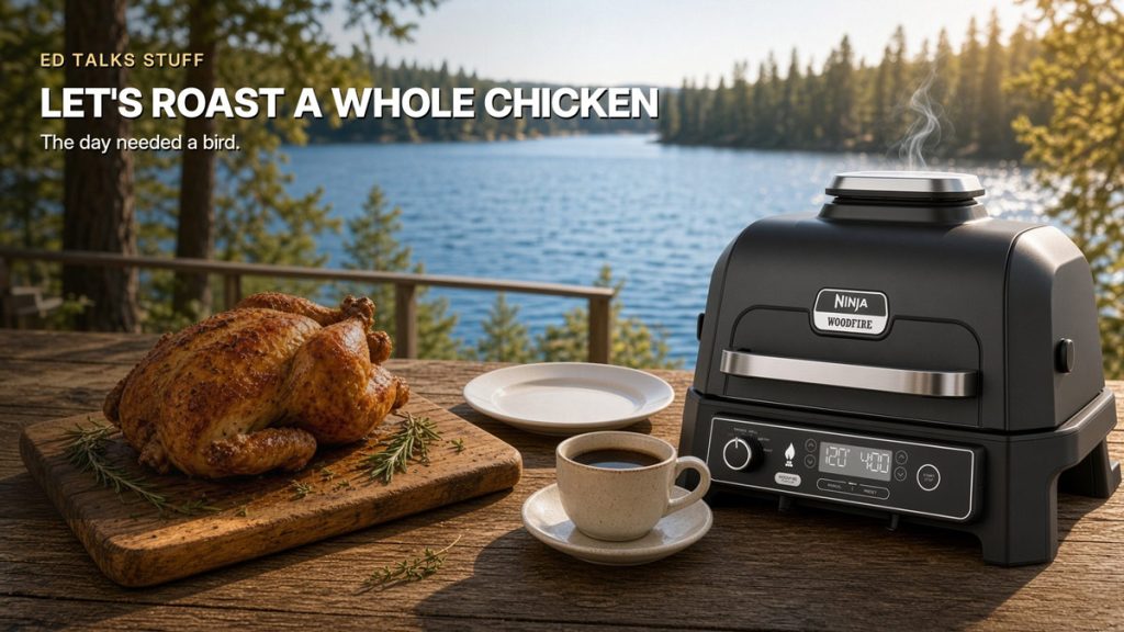 A roasted whole chicken on a wooden cutting board next to a cup of coffee and a black Ninja Woodfire electric grill outdoors with a lake and forest background, featuring overlay text that reads "ED TALKS STUFF - LET'S ROAST A WHOLE CHICKEN - The day needed a bird."